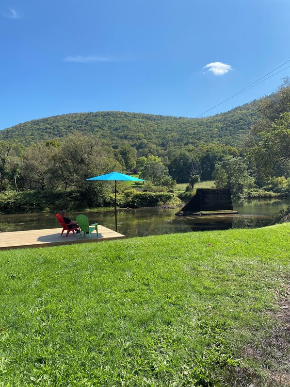 Une vue sur la rivière, avec un quai en bois, des chaises et un parasol bleu.