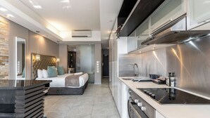 A modern hotel room with a large bed, a built-in kitchen with a stove and sink, and a stone accent wall. - Sleek Central Apartment | Wifi | Pool | Gym (Cape Town)