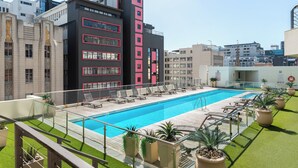A rooftop pool area with lounge chairs and a swimming pool, surrounded by buildings with modern architecture. - Sleek Central Apartment | Wifi | Pool | Gym (Cape Town)
