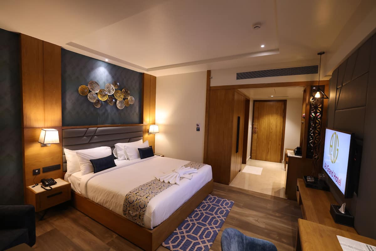 A modern hotel room with a large bed, bedside lamps, a TV, and a decorative wall piece.