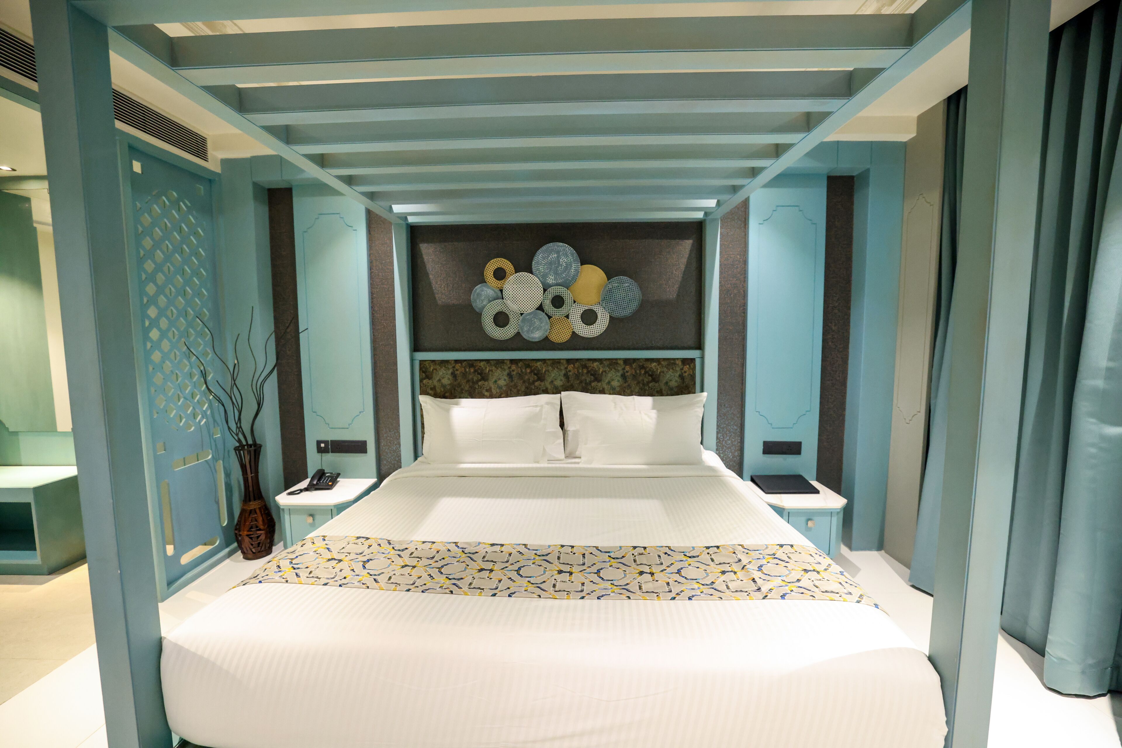 Ein modernes Hotelzimmer mit einem großen Bett, einem dekorativen Wandbild darüber und einem kleinen Nachttischchen mit einem Telefon.