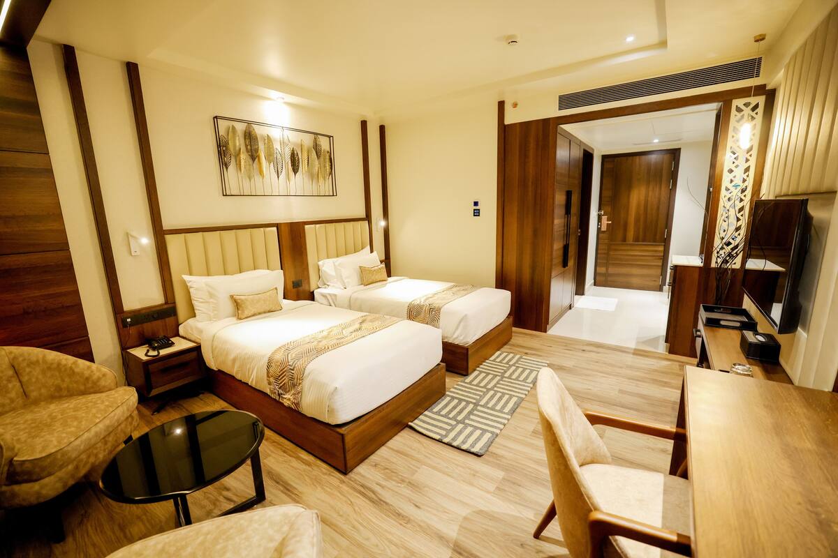 A hotel room with two beds, a desk, a chair, a TV, and a decorative wall piece.