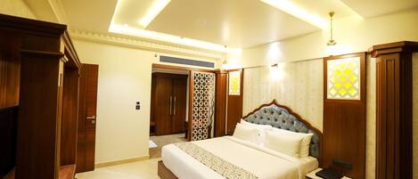 A well-lit bedroom with a large bed, wooden wardrobe, and a small bedside table.