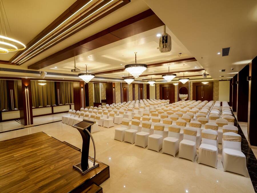 A large conference room with rows of white chairs, a podium, and chandeliers.