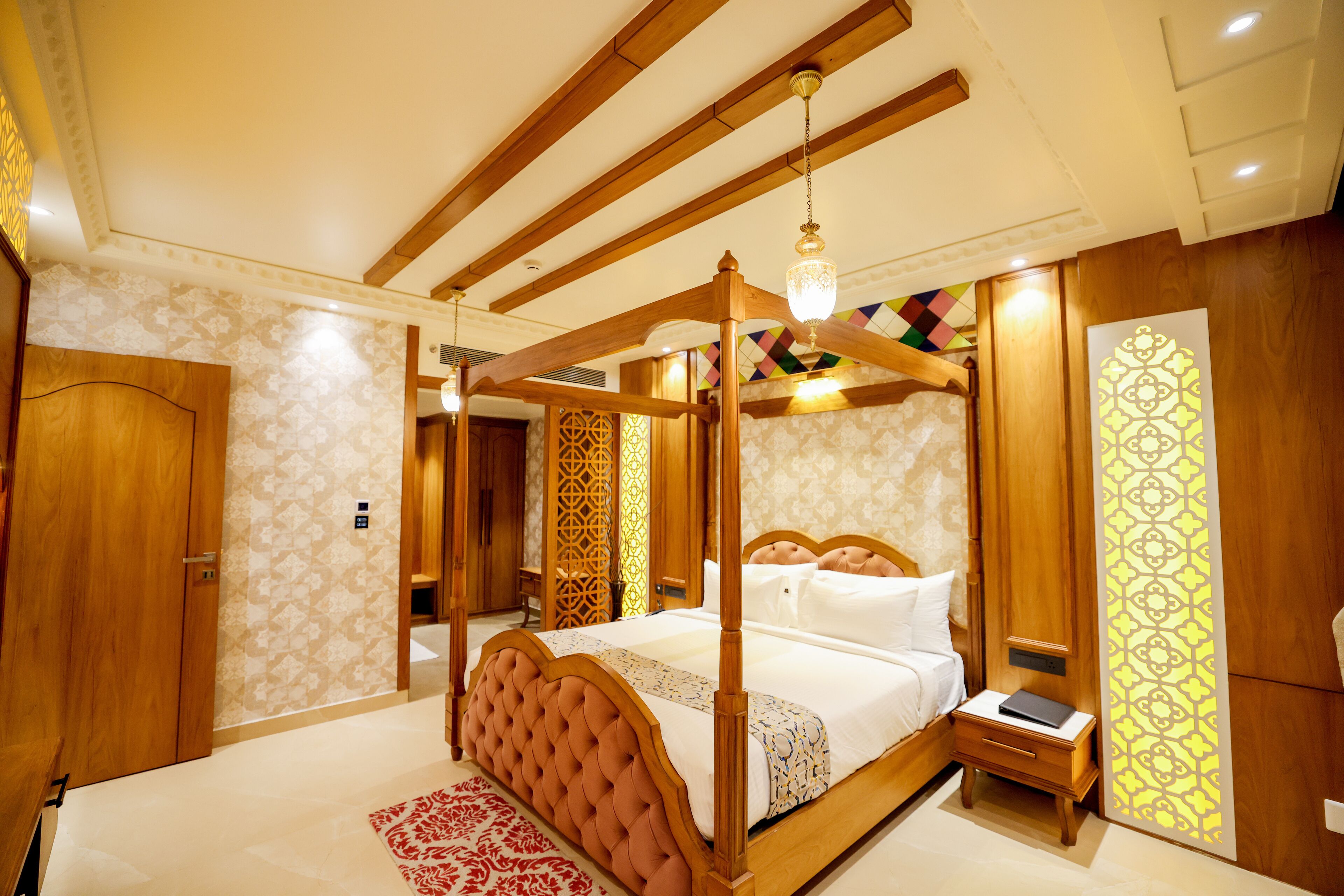 A four-poster bed with a wooden frame and a canopy, a bedside table with a book, and a patterned wall.
