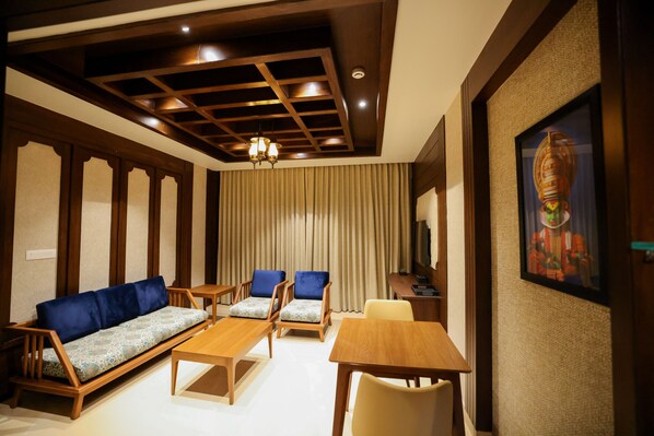Habitación de hotel con techo de madera, un sofá, dos sillas, una mesa y un televisor.