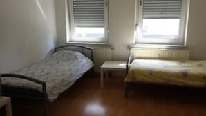 Une petite chambre avec deux lits simples, une petite table et un radiateur.