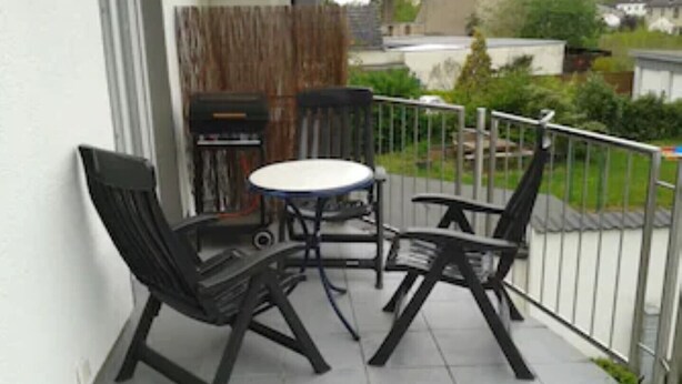 Une petite terrasse extérieure avec une table ronde et deux chaises, une clôture en bois et une vue sur un quartier résidentiel.