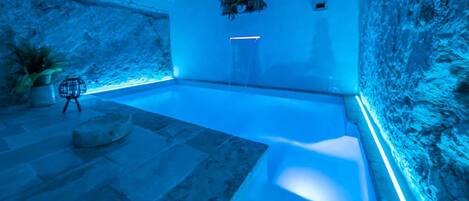Un área interior de piscina moderna con suelo de piedra, zona de estar y una planta en la pared.