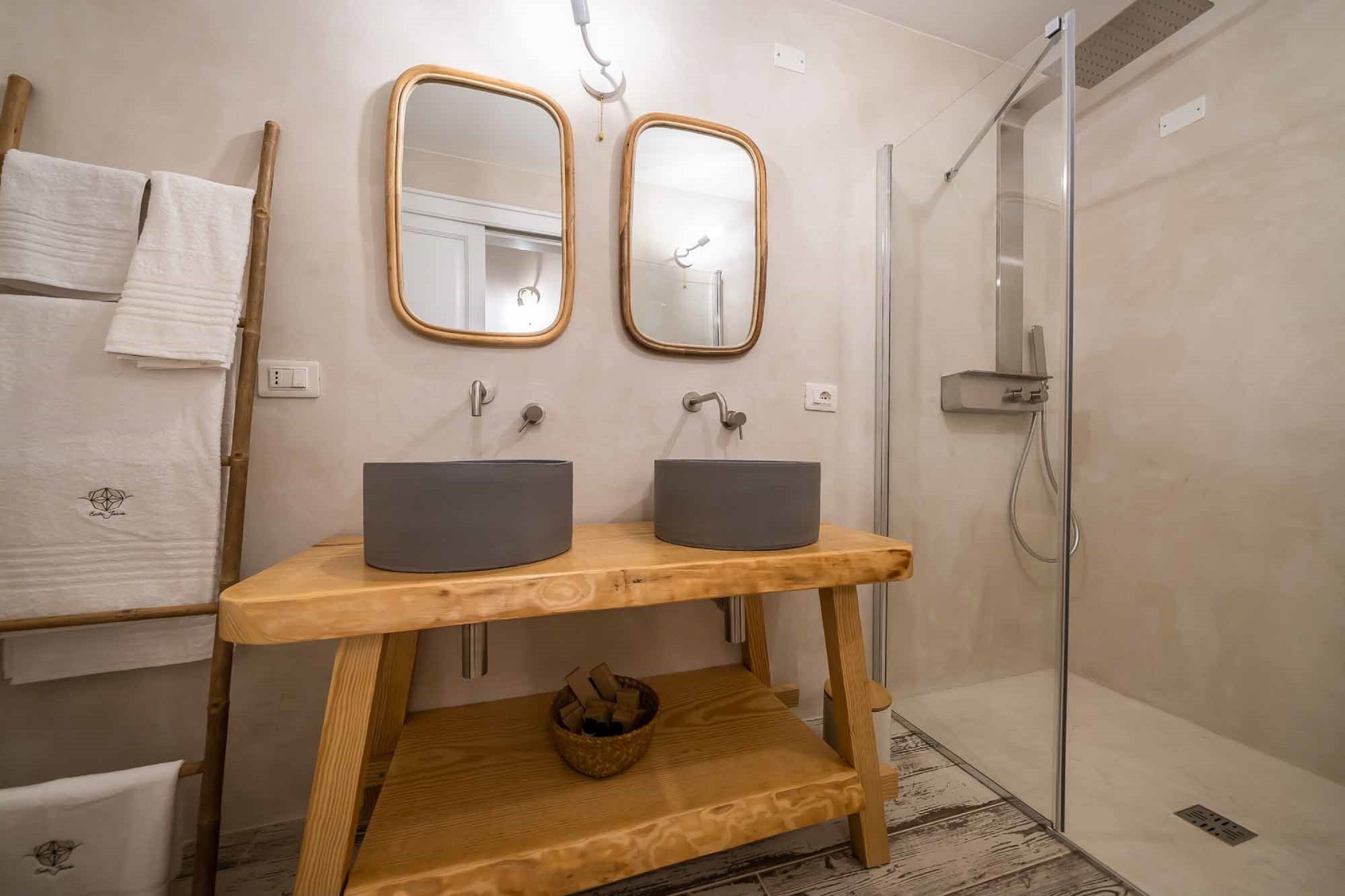 Un baño con dos lavamanos, tocador de madera, espejos y ducha.