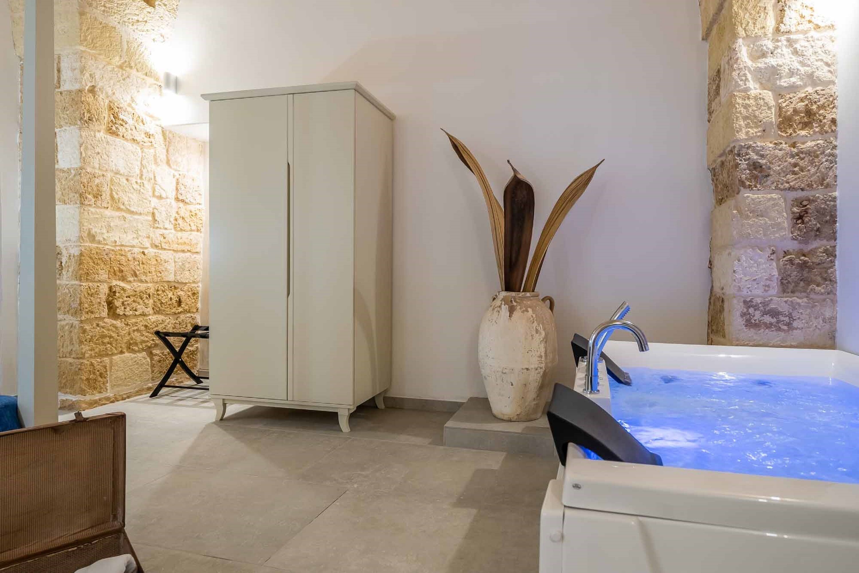 Ein Badezimmer mit Steinwand, einem weißen Schrank, einer großen Vase mit Pflanzen und einer Badewanne mit fließendem Wasser.