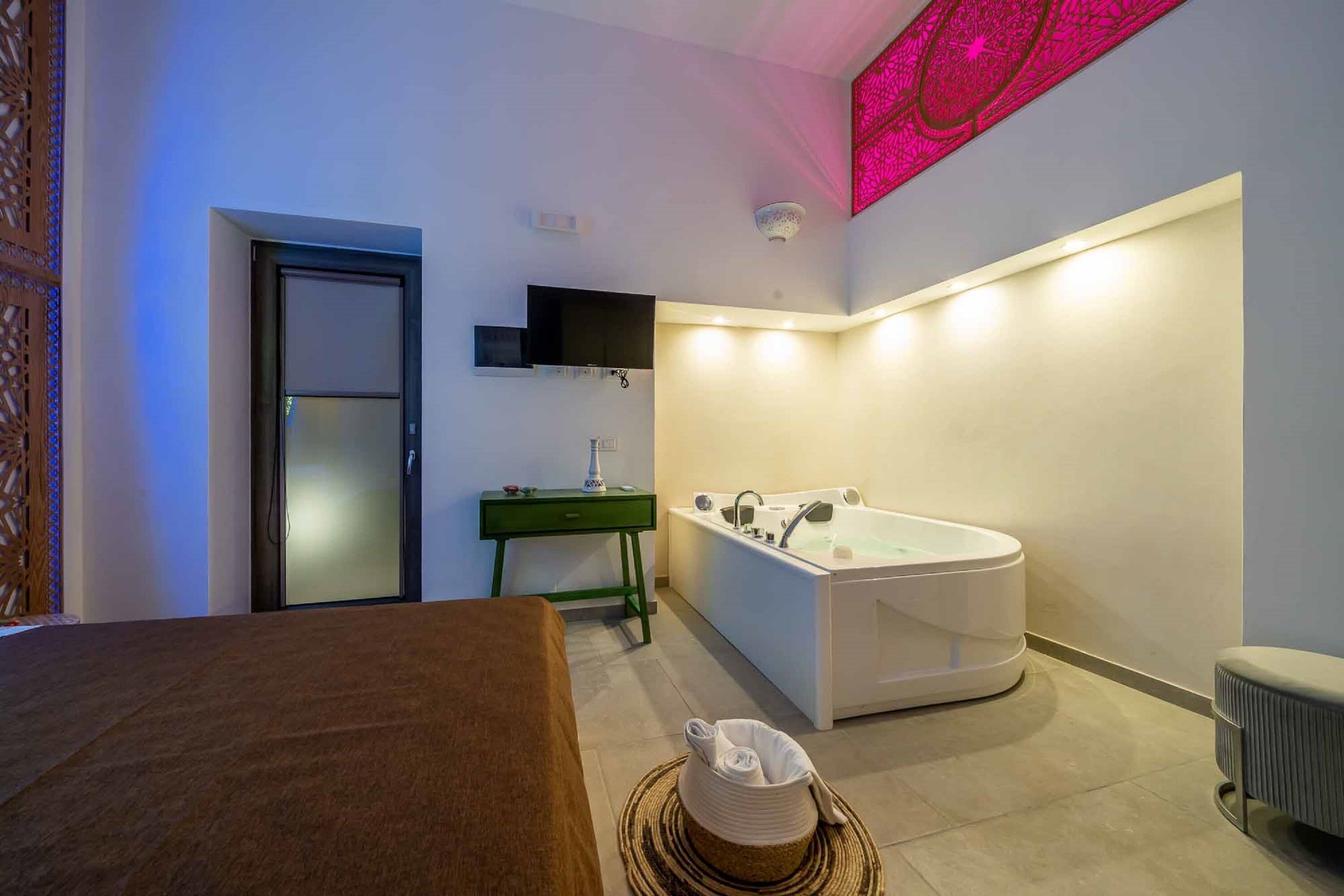 Une salle de bain moderne avec une grande baignoire, un meuble-lavabo vert et un téléviseur fixé au mur.