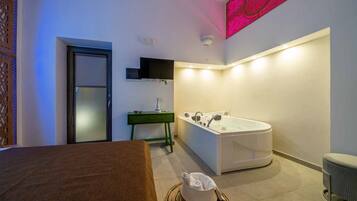 Une salle de bain moderne avec une grande baignoire, un meuble-lavabo vert et un téléviseur fixé au mur.