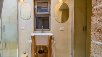 A bathroom with a wooden vanity, two wall-mounted mirrors, a window with curtains, and a shower area.
