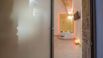 A modern bathroom with a stone wall, a curved bathtub, and a mounted TV.