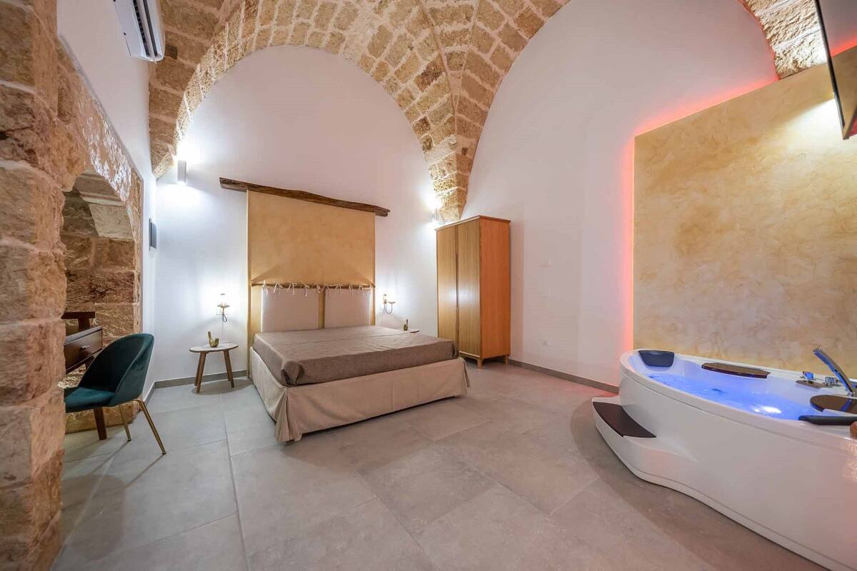 Ein Schlafzimmer mit Bett, einem kleinen Tisch, einem Sessel, einem Kleiderschrank und einer Badewanne.