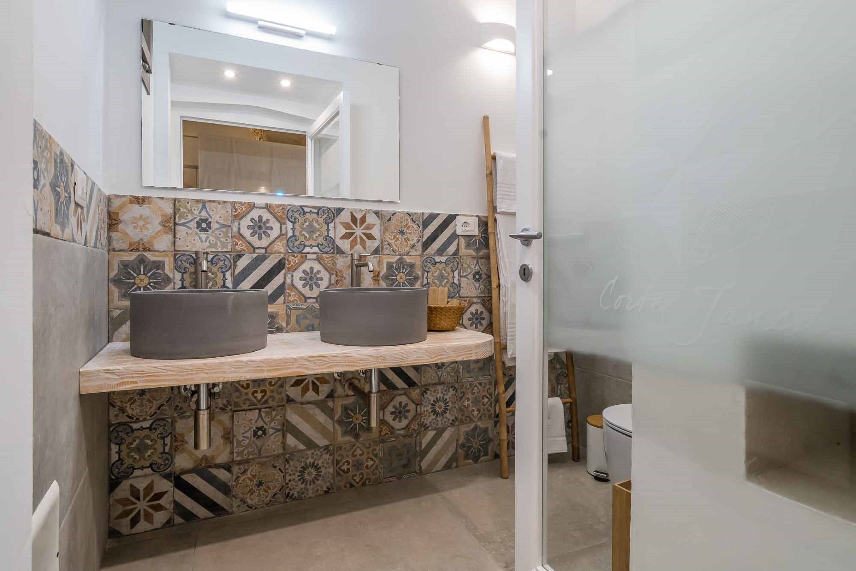Une salle de bain avec deux lavabos, un miroir et un mur recouvert de carreaux.