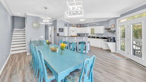 A dining area with a blue table and chairs, a kitchen in the background, and a staircase to the left. - Starfish Retreat II  Walk to Carolina Beach (Carolina Beach)