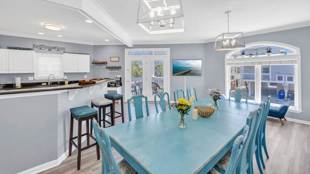 A spacious kitchen with a central island, a dining area with blue chairs, and a large window with a view. - Starfish Retreat II  Walk to Carolina Beach (Carolina Beach)