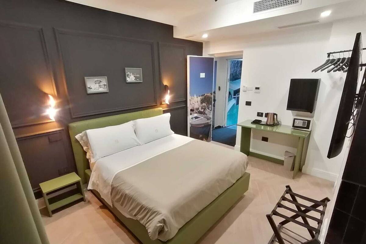 A modern hotel room with a large bed, a small desk with a microwave, a TV, and a balcony with a view.