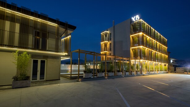 A modern hotel with a prominent 'XB' sign, featuring a glass facade, outdoor seating area, and a spacious courtyard. - X Business (Saviano)