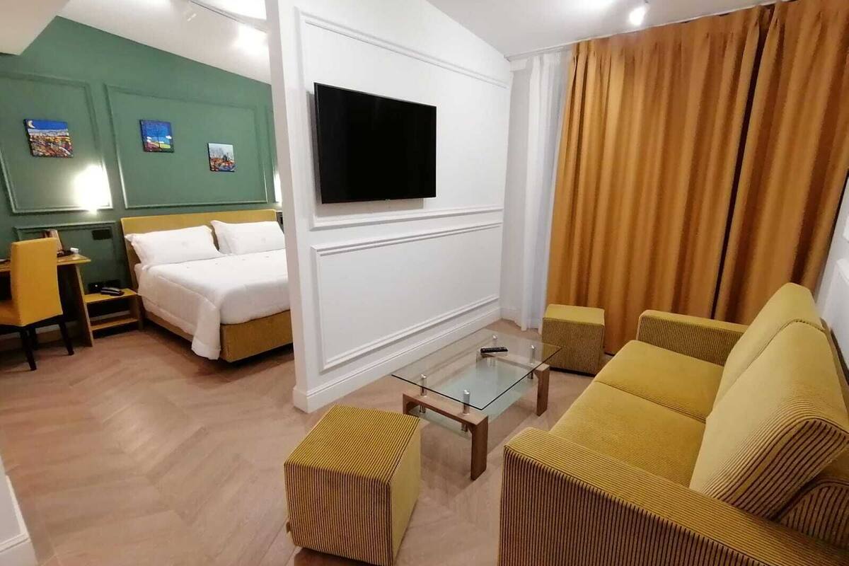 A modern hotel room with a bed, a sofa, a TV, and a desk.