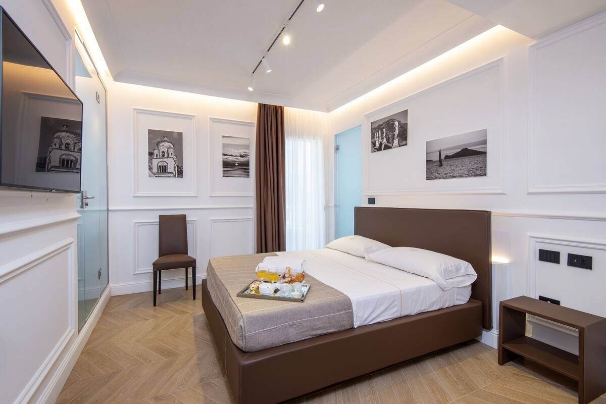 A modern hotel room with a large bed, a chair, and a tray with breakfast items.
