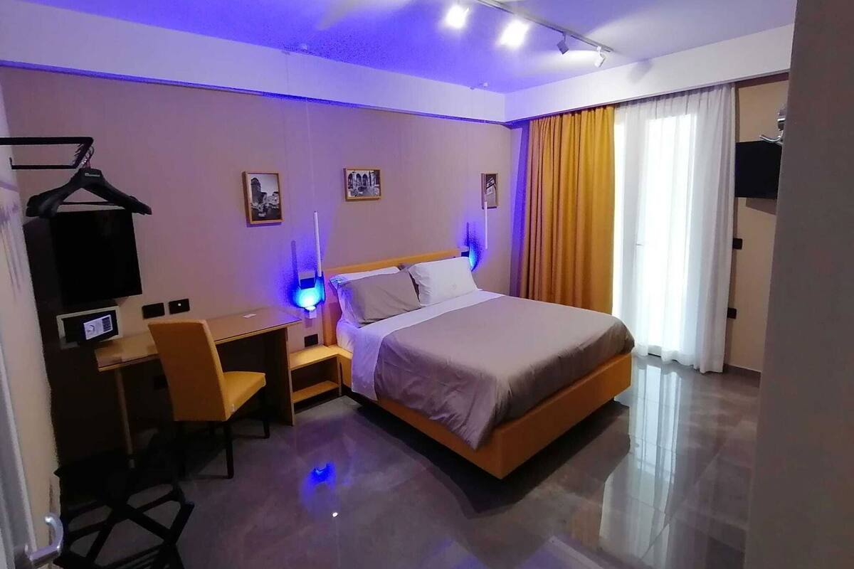 A hotel room with a bed, desk, chair, and a TV on the wall.