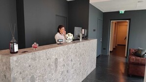 A reception desk with a marble counter, a receptionist, a desktop computer, a phone, and a vase with flowers. - X Business (Saviano)