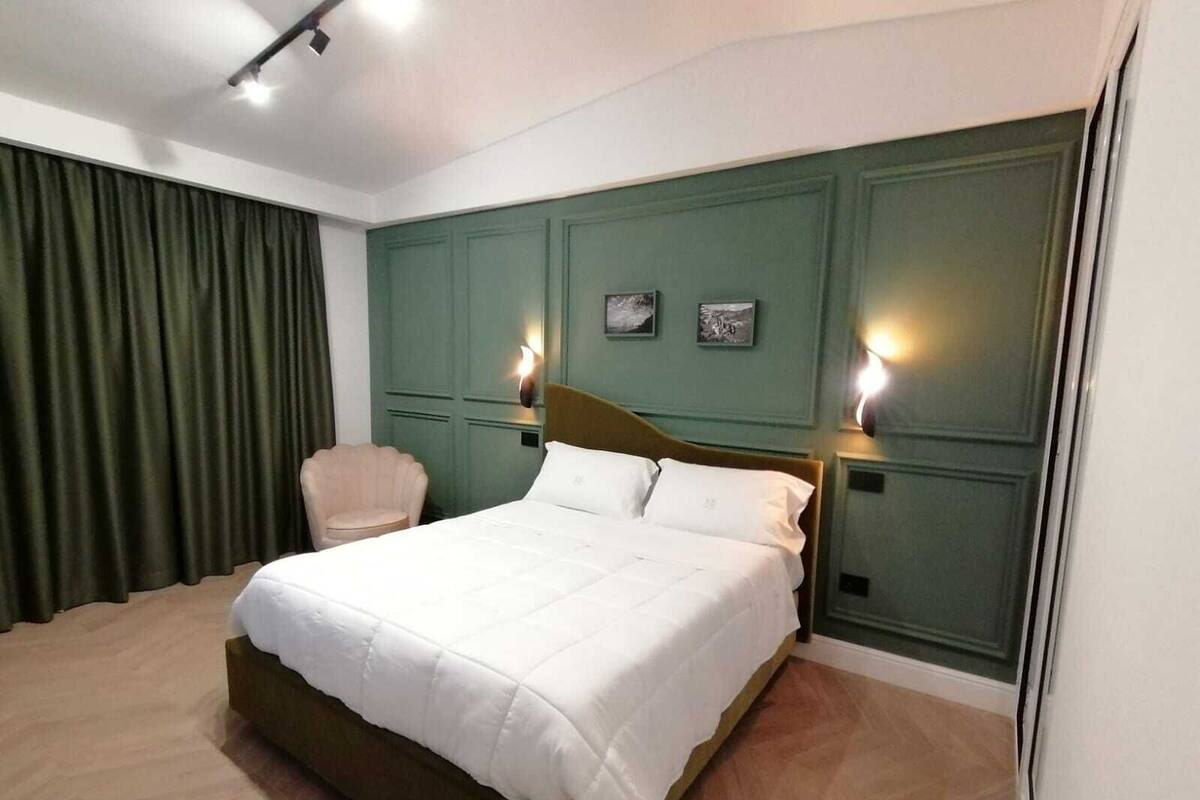 A bedroom with a large bed, a chair, and two wall-mounted lights.