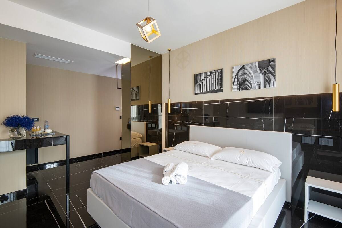 A modern hotel room with a large bed, a bedside table with a vase of flowers, and a mirror.