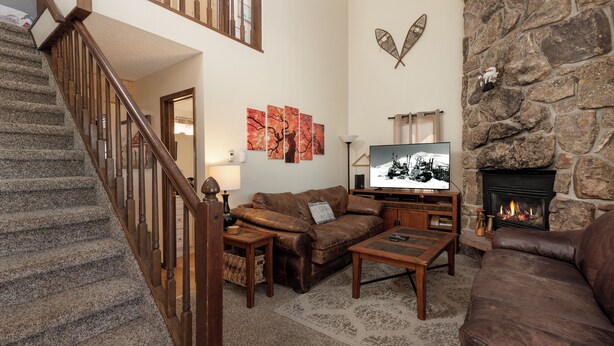 A living room with a stone fireplace, a television, a brown leather sofa, and a staircase. - Twin Rivers Vasquez 3 Perfect 3 Bedroom sleeps 9, private deck, river views (Fraser)