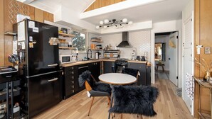 A modern kitchen with a black refrigerator, wooden cabinets, and a round dining table with black furry chairs. - BeeHive Bungalow - Gorgeous Lake views and completely updated throughout! (Grand Lake)