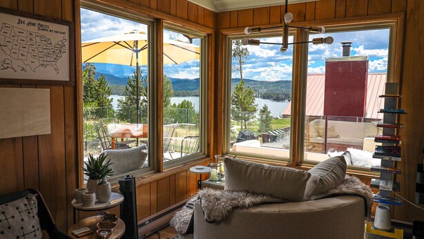 A cozy cabin interior with large windows offering a view of a lake and mountains. - BeeHive Bungalow - Gorgeous Lake views and completely updated throughout! (Grand Lake)