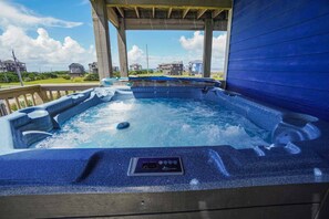 A hot tub with a control panel, surrounded by a wooden deck and a blue wall, with houses visible in the background. - Oceanfront Home with Private Pool, Hot Tub, Elevator and Wet Bar (Frisco)