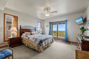 A bedroom with a bed, bedside lamps, a ceiling fan, a TV, a balcony with a view, and a wooden dresser. - Oceanfront Home with Private Pool, Hot Tub, Elevator and Wet Bar (Frisco)