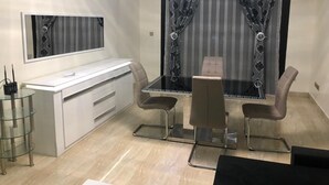 Ein modernes Zimmer mit Glastisch, zwei Stühlen, einem weißen Schreibtisch und einem Spiegel.