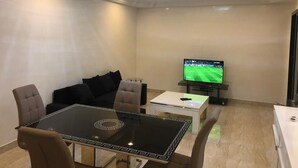 Ein modernes Wohnzimmer mit einem Esstisch mit Glasplatte, einer Couch, einem Fernseher und einer Deckenleuchte.