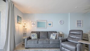 Een woonkamer met een grijze bank, een leren fauteuil, een bijzettafeltje en een vloerkleed.