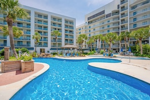 A hotel with multiple balconies, a swimming pool, and palm trees.