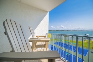 A balcony with a view of a tennis court and water.