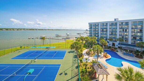 Een hotel met een tennisbaan, zwembad en uitzicht op het water.