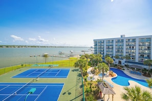 A hotel with a tennis court, pool, and waterfront view.