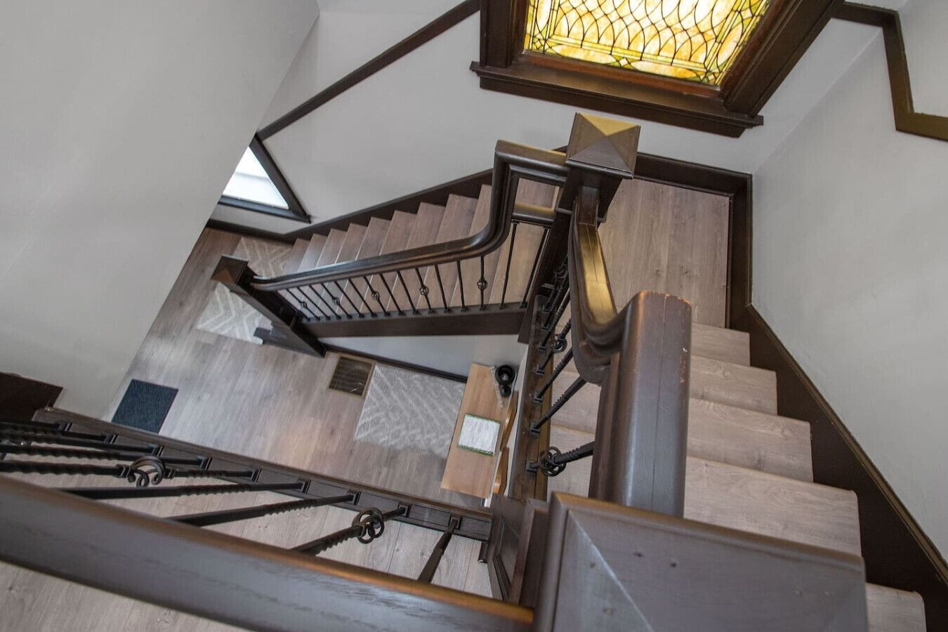 A wooden staircase with a metal handrail and a stained glass window above.