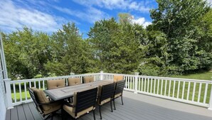 A deck with a dining table and chairs, surrounded by a white railing, set against a backdrop of trees and a clear sky. - Beautiful Comfortable House w/ Fireplace (Woodstock)