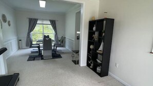 A spacious room with a large window, a black bookshelf, and a dining area with a table and chairs. - Beautiful Comfortable House w/ Fireplace (Woodstock)