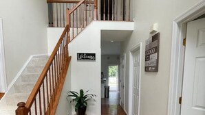 A spacious hallway with a wooden staircase leading to a second floor. A welcome sign and a 'Good to See You' sign are visible on the walls. - Beautiful Comfortable House w/ Fireplace (Woodstock)