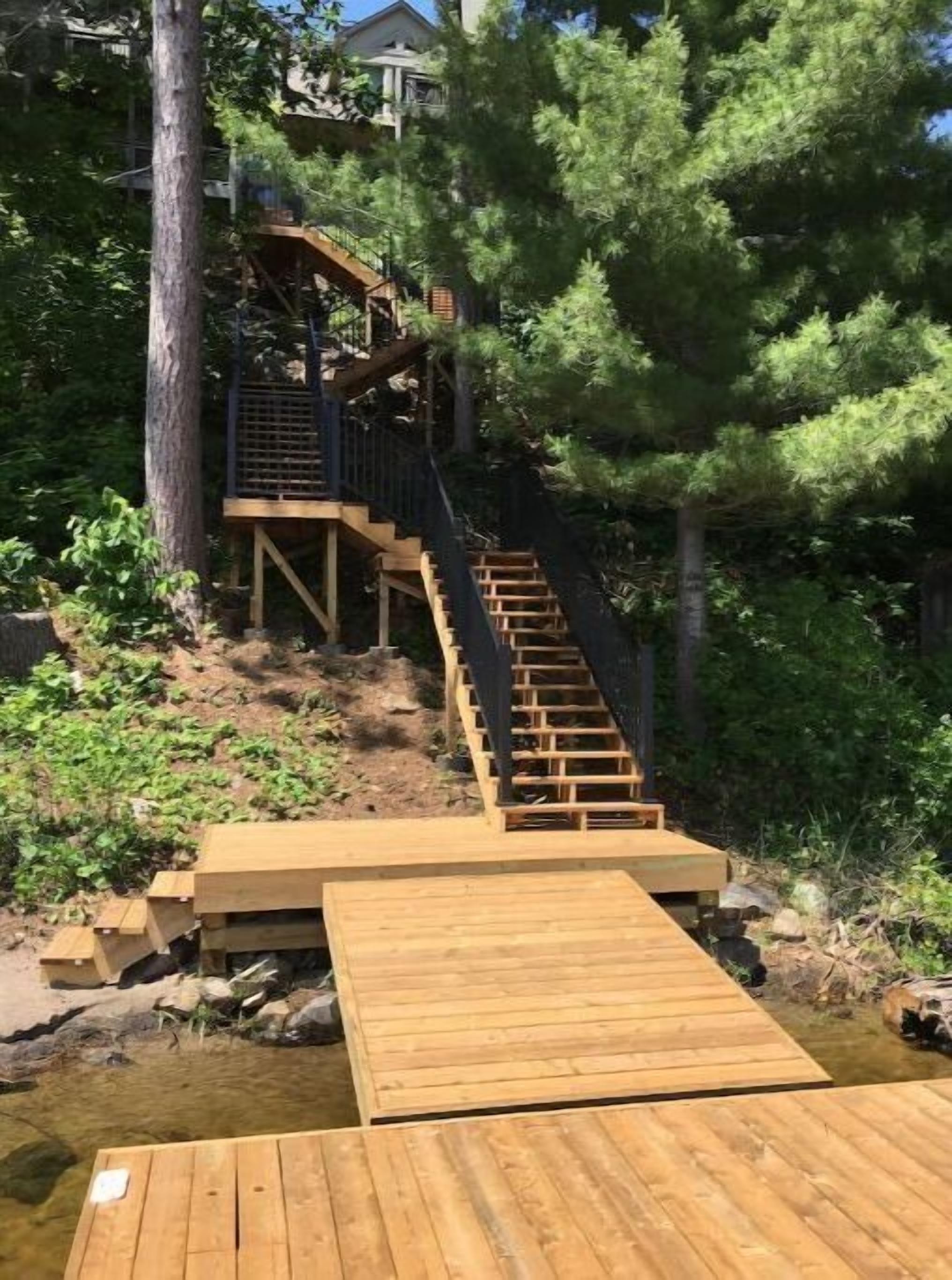 Une terrasse en bois avec un escalier menant à une plateforme, le tout entouré d’arbres.