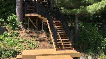Une terrasse en bois avec un escalier menant à une plateforme, le tout entouré d’arbres.