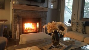 A living room with a fireplace, a sofa, a coffee table with a vase of flowers, and a television mounted on the wall.